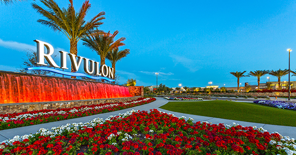 water feature with rivulon sign and palm trees at dusk